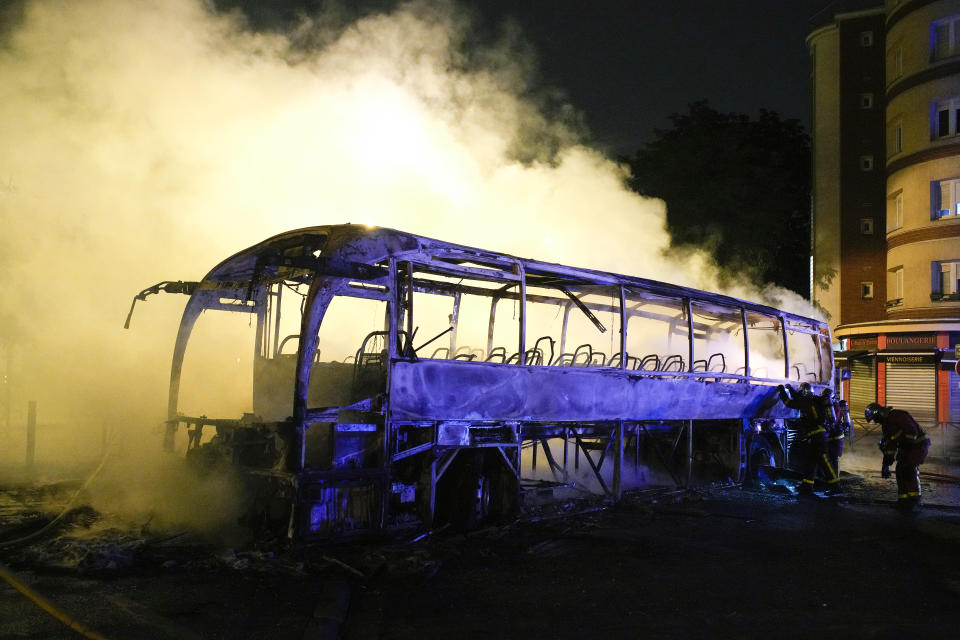 Firefighters use a water hose on a burnt bus in Nanterre, outside Paris, France, Saturday, July 1, 2023. French President Emmanuel Macron urged parents Friday to keep teenagers at home and proposed restrictions on social media to quell rioting spreading across France over the fatal police shooting of a 17-year-old driver. (AP Photo/Lewis Joly)