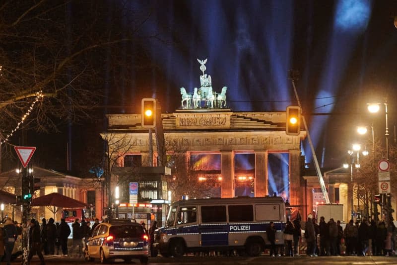 People walk towards the colorfully illuminated Brandenburg Gate while police cars drive past during an event marking the New Year's Eve. Annette Riedl/dpa