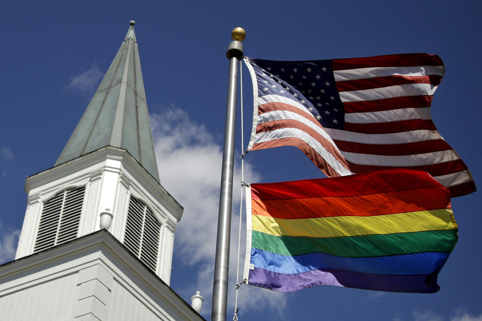 FILE - In this April 19, 2019 file photo, a gay pride rainbow flag flies along with the U.S. flag in front of the Asbury United Methodist Church in Prairie Village, Kan. Had there been no COVID-19 coronavirus pandemic, America’s largest mainline Protestant denomination would be convening in May 2020 for a likely vote on breaking up over differences on same-sex marriage and ordination of LGBTQ pastors. (AP Photo/Charlie Riedel, File)