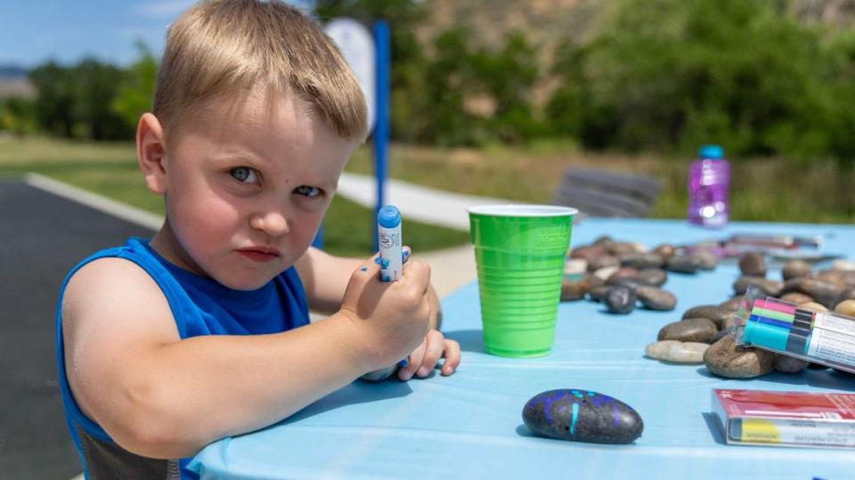 Olympus Winn, 3, decorates rocks at a children’s table while attending the Central Foothills Neighborhood Association’s block party with his mother, Sara Winn.