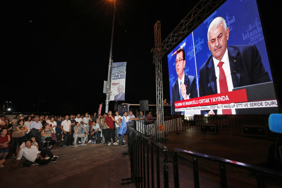 People watch a live broadcast of a televised debate between Istanbul's mayoral candidate Binali Yildirim, right, of Turkey's ruling Justice and Development Party, or AKP, and Ekrem Imamoglu, centre, candidate of the secular opposition Republican People's Party, or CHP, ahead of June 23 re-run of Istanbul elections, Sunday, June 16, 2019. Televised election debates are uncommon in Turkey. The last one, between AKP leader Recep Tayyip Erdogan and the then-leader of the CHP, took place before a 2002. The AKP has been in power since. (AP Photo/Emrah Gurel)