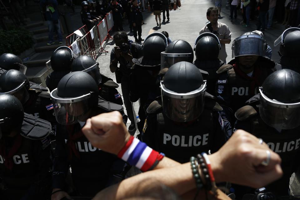 An anti-government protester gestures towards anti-riot policemen outside the headquarters of the ruling Puea Thai Party of Prime Minister Yingluck Shinawatra in Bangkok