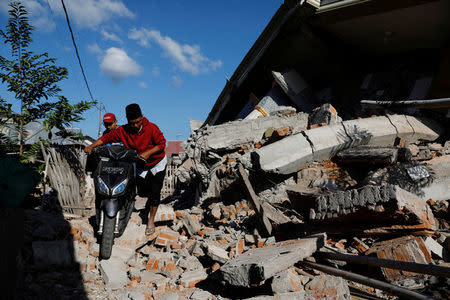 People push their motorcycle through the collapsed ruins of a mosque after an earthquake hit on Sunday in Pemenang, Lombok island, Indonesia, August 7, 2018. REUTERS/Beawiharta