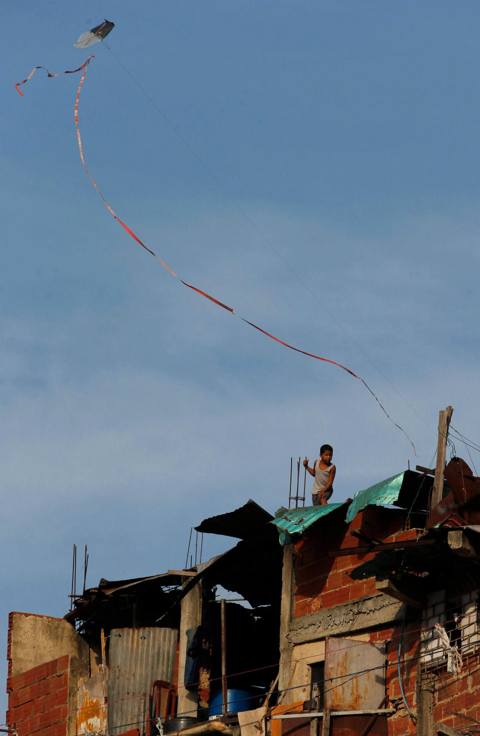 En esta foto del 27 de marzo de 2014, un niño eleva una cometa desde la techumbre de su casa en el suburbio de Petare, donde trabajan doctores cubanos. Muchos de los habitantes de Petare han sido atendidos por doctores cubanos en un programa gratuito gracias a un convenio con el gobierno venezolano. (AP Photo/Fernando Llano)