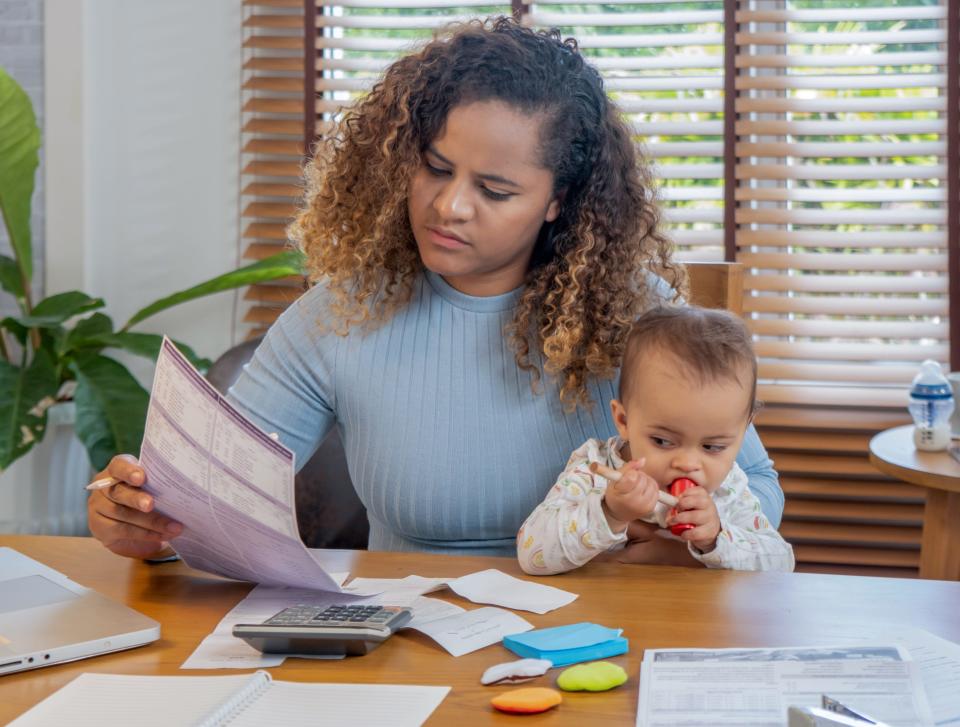 Mother reading monthly budget while holding baby.