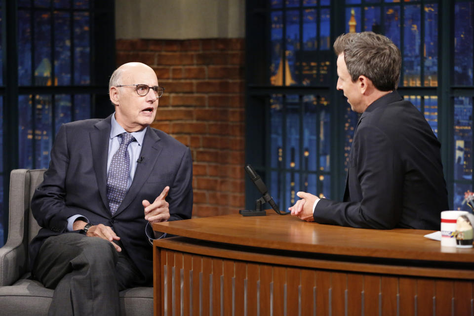 Jeffrey Tambor in a business suit and tie having an animated discussion with Seth Meyers, who is also in a suit, on a late-night talk show set