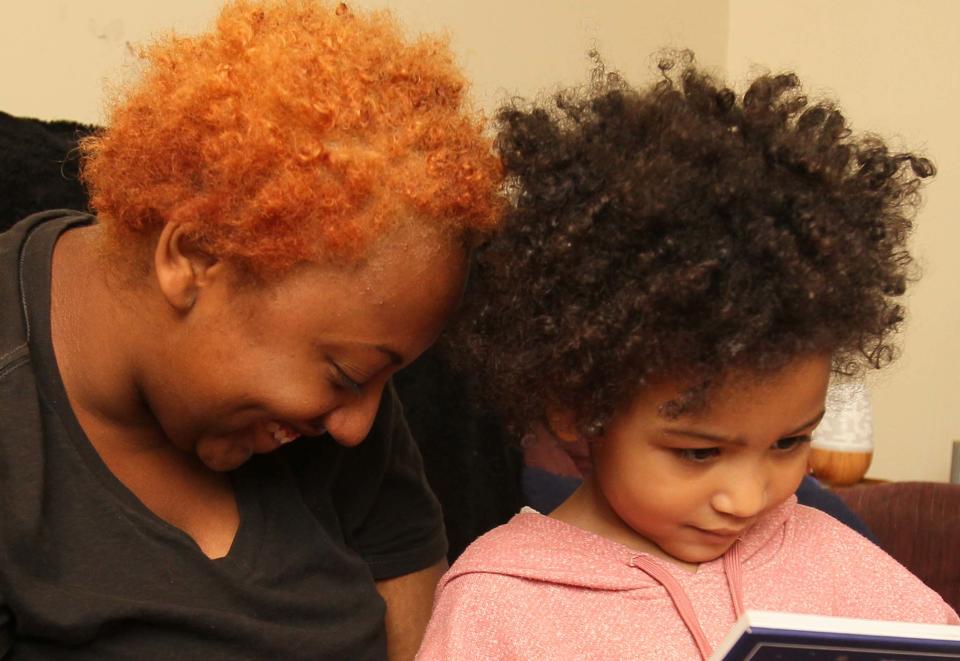 Jasmine Kirk hugs her daughter Luna as she looks at a book in their home in Akron.