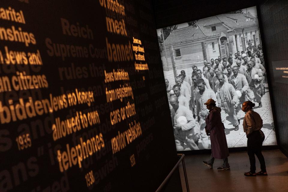 People walk passed phrases from laws by Nazis that systematically limited the rights and freedoms of Jewish people through a section of an exhibit at The Holocaust Center in Farmington Hills on Friday, May 10, 2024.