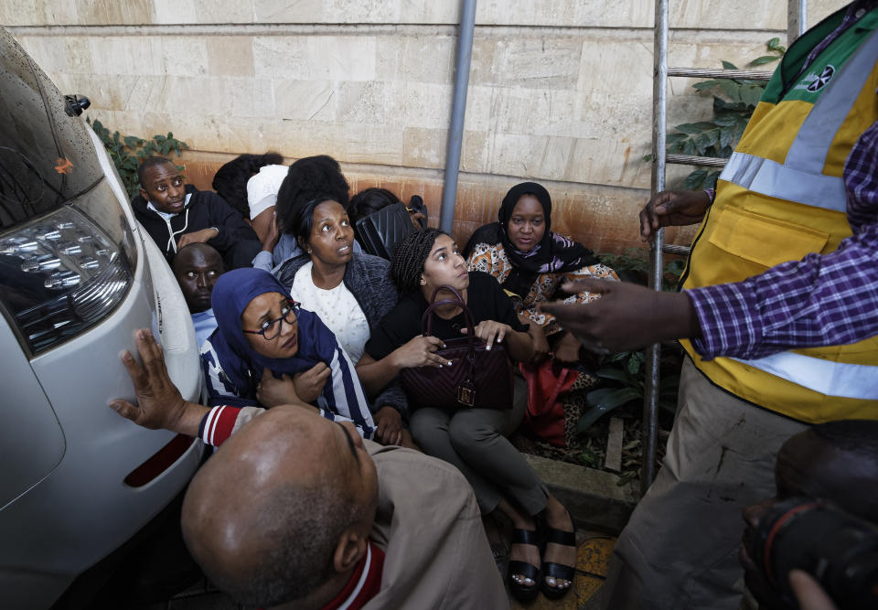 Civilians huddle between cars as the sound of gunshots are heard at a hotel complex in Nairobi, Kenya Tuesday, Jan. 15, 2019. Terrorists attacked an upscale hotel complex in Kenya's capital Tuesday, sending people fleeing in panic as explosions and heavy gunfire reverberated through the neighborhood. (AP Photo/Ben Curtis)