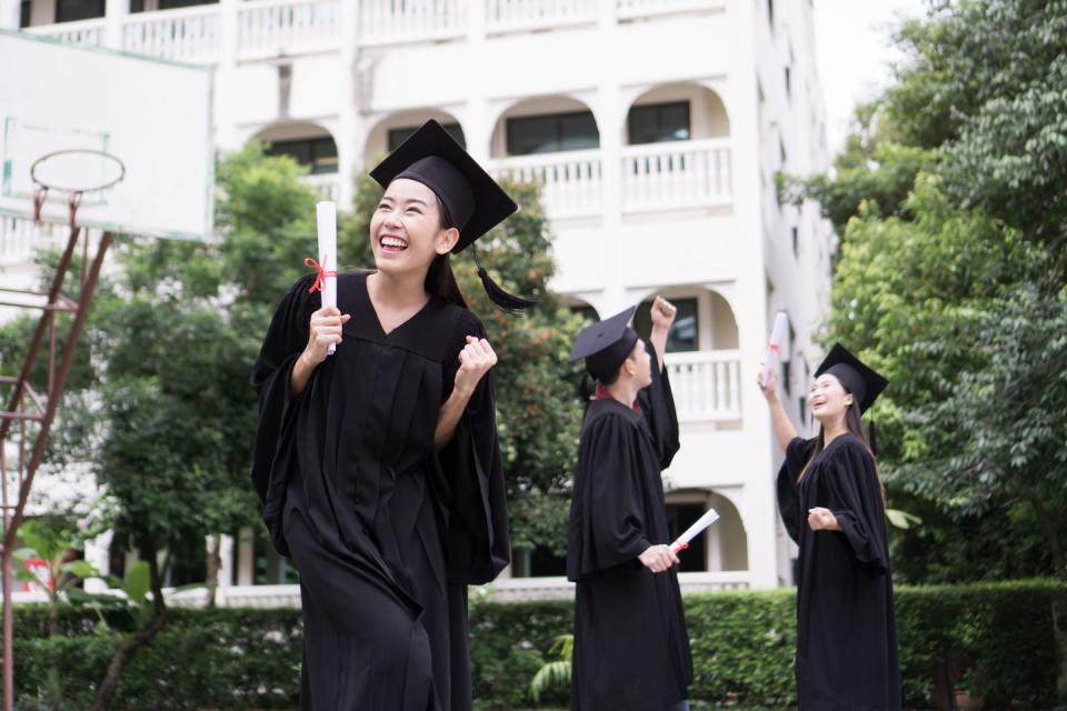 cheerful student with clenched fist wearing graduation gown