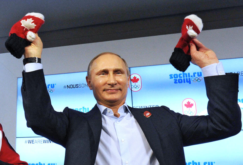 Russian President Vladimir Putin shows handmade mittens presented to him at Canada House during the 2014 Winter Olympics, Friday, Feb. 14, 2014 in Sochi, Russia. At left is Chairman of the Canadian National Olympic Committee Marcel Aubut. (AP Photo / RIA-Novosti, Mikhail Klimentyev, Presidential Press Service)