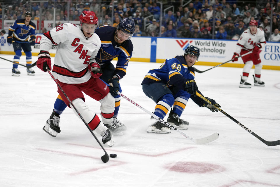 Carolina Hurricanes' Sebastian Aho (20) reaches for a loose puck as St. Louis Blues' Zack Bolduc (76) and Scott Perunovich (48) defend during the third period of an NHL hockey game Friday, April 12, 2024, in St. Louis. (AP Photo/Jeff Roberson)
