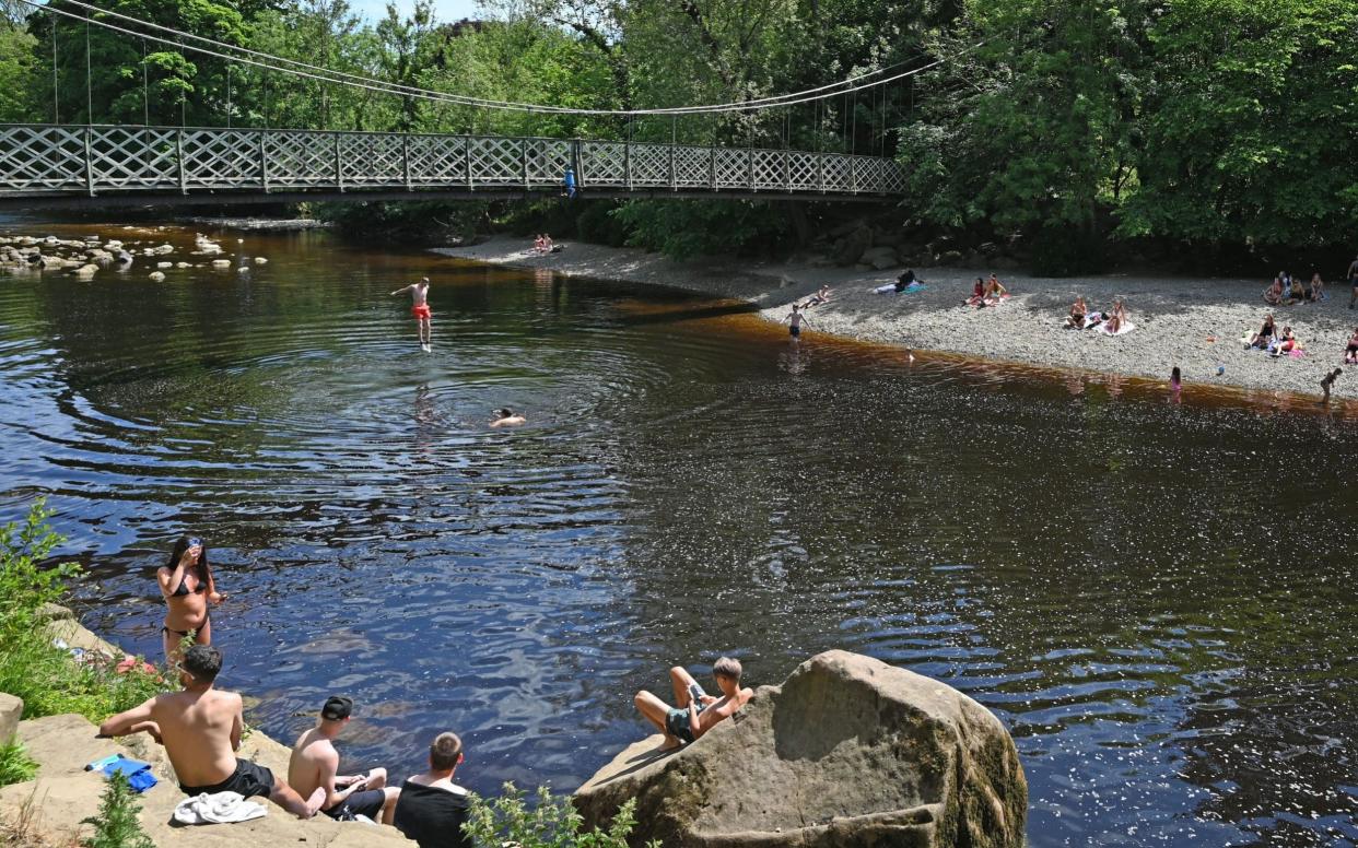 A man jumps from the suspension bridge into the water as others relax on the banks of the River Wharfe in Ilkley - PAUL ELLIS/AFP