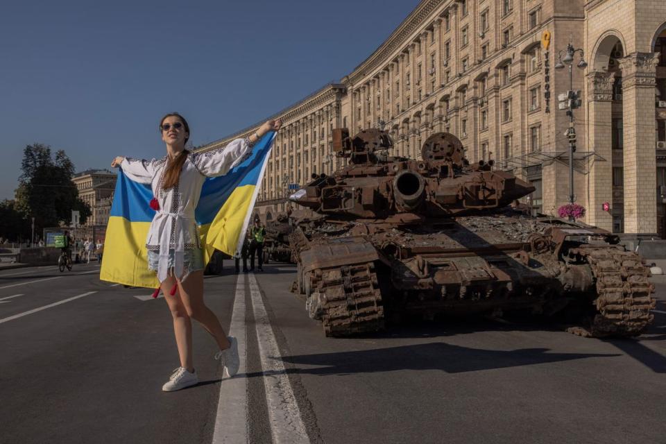 A woman poses for photos holding the Ukrainian flag next to destroyed Russian armoured military vehicles on display in Khreshchatyk Street on Ukraine's Independence Day in Kyiv, on August 24, 2023, amid the Russian invasion of Ukraine. (Photo by Roman Pilipey / AFP) (Photo by ROMAN PILIPEY/AFP via Getty Images)