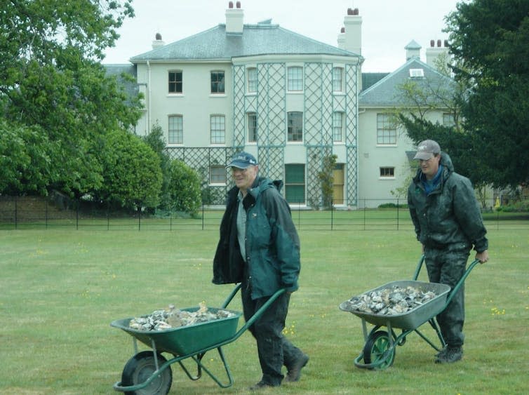 Two men moving flints in wheelbarrows.