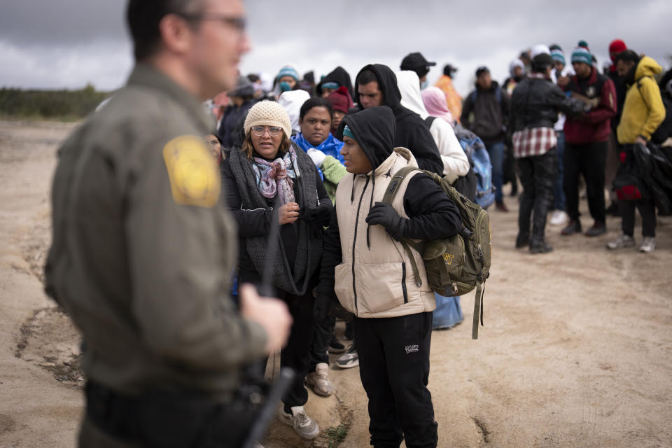 La peruana Julia Paredes, en el centro con un gorro blanco, escucha las instrucciones de un agente de la Patrulla Fronteriza con otros solicitantes de asilo mientras esperan a ser procesados tras cruzar la cercana frontera con México, el jueves 25 de abril de 2024 en Boulevard, California. México empezó a requerir visas a los peruanos en respuesta al aluvión de migrantes del país suramericano, tras tomar medidas idénticas para venezolanos, ecuatorianos y brasileños, lo que en la práctica eliminó la opción de viajar en avión a una ciudad mexicana cerca de la frontera estadounidense. (AP Foto/Gregory Bull)