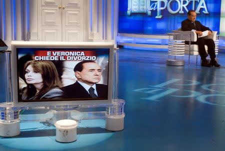 FILE PHOTO: Italy's Prime Minister Silvio Berlusconi sits near a television monitor showing images of him and his wife Veronica Lario during the taping of television program Porta a Porta ("Door to door") in Rome, Italy May 5, 2009. REUTERS/Remo Casilli/File Photo