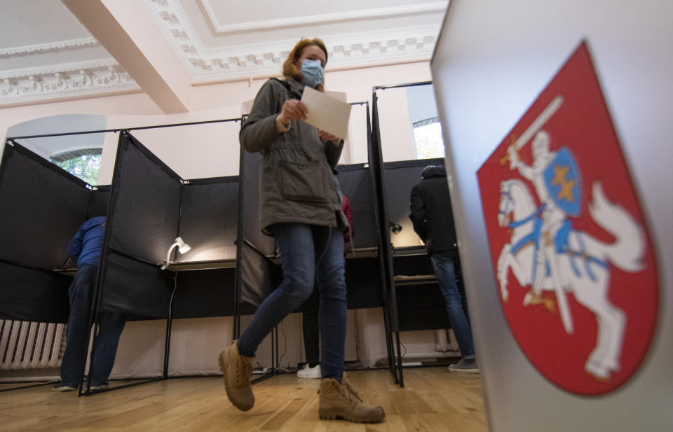 A woman, wearing face masks to protect against coronavirus walks to cast their ballots at a polling station during parliamentary elections in Vilnius, Lithuania, Sunday, Oct.11, 2020. Polls opened Sunday for the first round of national election in Lithuania, where voters will renew the 141-seat parliament and the ruling four-party coalition is widely expected to face a stiff challenge from the opposition to remain in office. (AP Photo/Mindaugas Kulbis)