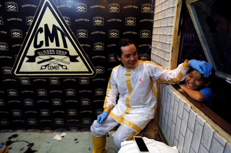 Herman Maulanasyah, a 40-year-old hair stylist, jokes with his son after giving a haircut to a customer while wearing a handmade protective suit in a tribute to the country's medical workers tackling the coronavirus disease (COVID-19) in Bogor