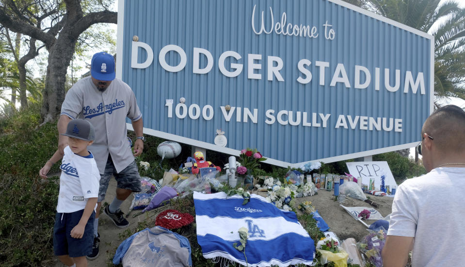 Los Angeles Dodger fans, including Rudy Escobar with his son Rodolofo, 7, visit a memorial for Los Angeles Dodgers broadcaster Vin Scully at the entrance to Dodger Stadium on Wednesday, Aug. 3, 2022, in Los Angeles. The Hall of Fame broadcaster, whose dulcet tones provided the soundtrack of summer while entertaining and informing Dodgers fans in Brooklyn and Los Angeles for 67 years, died Tuesday night. He was 94. (Dean Musgrove/The Orange County Register via AP)