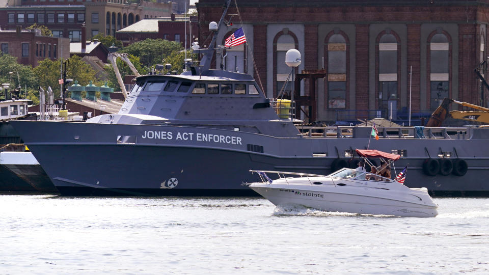 A boat passes the vessel Jones Act Enforcer, along the waterfront, Tuesday, July 11, 2023, in New Bedford, Mass. The trade association that represents the offshore service industry is going to great lengths to make sure that jobs go to Americans as the U.S. offshore wind industry ramps up. (AP Photo/Charles Krupa)