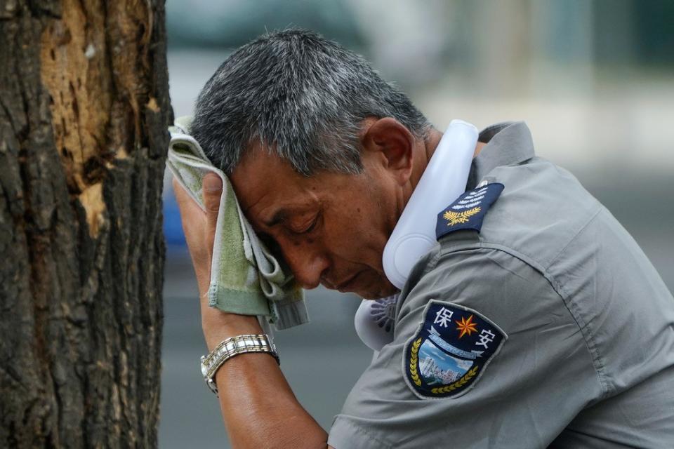 中國北京高溫，一位保安脖子上掛著電風扇並擦著汗。美聯社