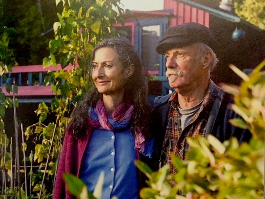 An older woman and man look onward, surrounded by plants.