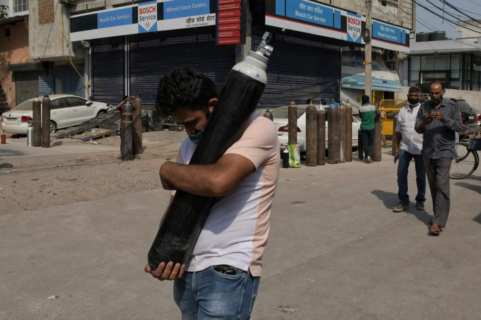 FILE - In this May 3, 2021, file photo, a man walks carrying a refilled cylinder as family members of COVID-19 patients wait in queue to refill their oxygen cylinders at Mayapuri area in New Delhi, India. COVID-19 infections and deaths are mounting with alarming speed in India with no end in sight to the crisis. People are dying because of shortages of bottled oxygen and hospital beds or because they couldn’t get a COVID-19 test. (AP Photo/Ishant Chauhan, File)