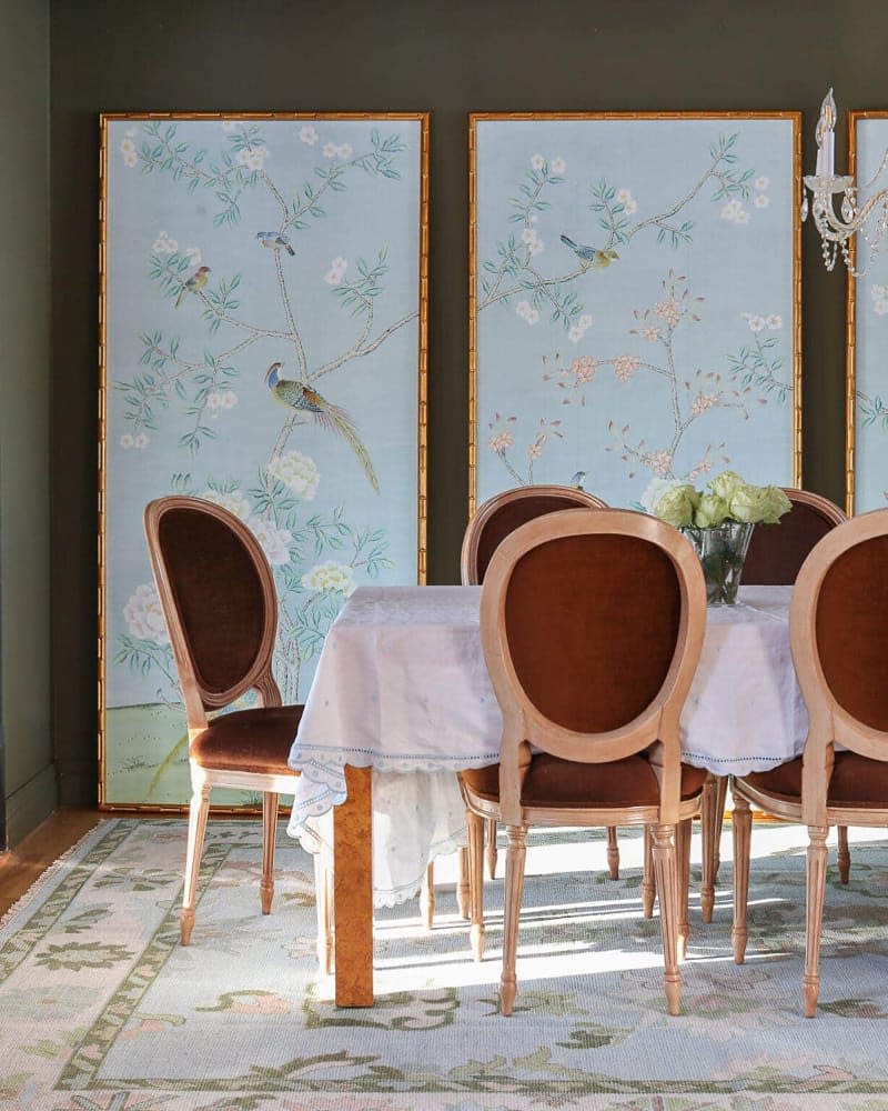 Framed wallpaper panels in dining room with wood and wine chairs.