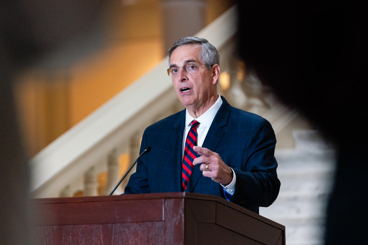 Secretary of State Brad Raffensperger at the podium, with a flight of marble steps behind him.