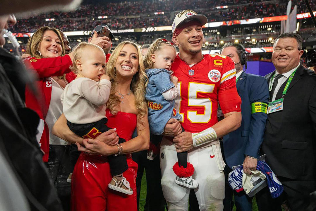 Brittany Mahomes and Patrick Mahomes with their young children smile on the field following the Chiefs Super Bowl win.