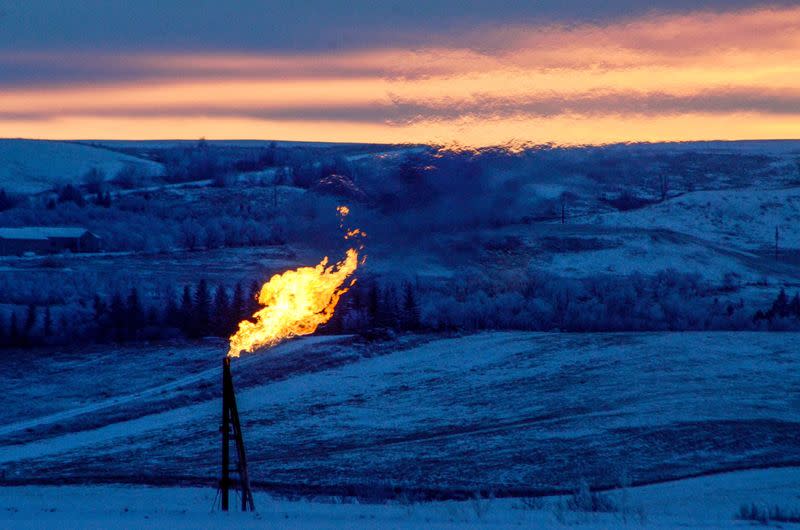 FILE PHOTO: A natural gas flare on an oil well pad burns as the sun sets outside Watford City, North Dakota