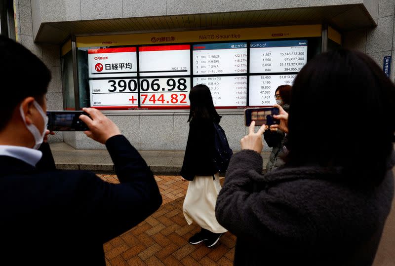 People using their smartphones take photos of electronic screens displaying Japan's Nikkei share average surged past an all-time record high scaled in December 1989 in Tokyo