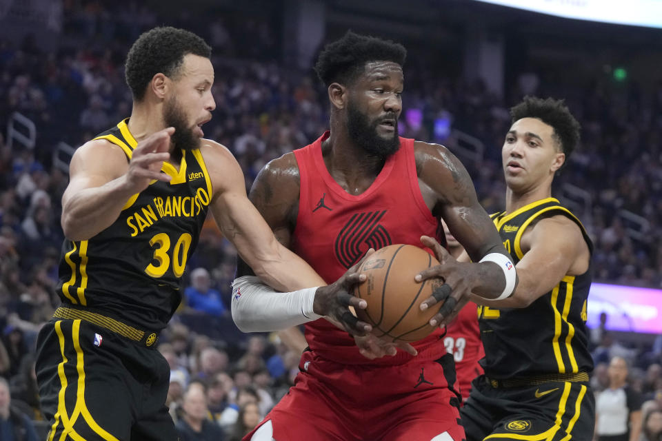 Portland Trail Blazers center Deandre Ayton, center, tries to turn toward the basket between Golden State Warriors guard Stephen Curry (30) and forward Trayce Jackson-Davis, right, during the first half of an NBA basketball game in San Francisco, Saturday, Dec. 23, 2023. (AP Photo/Jeff Chiu)