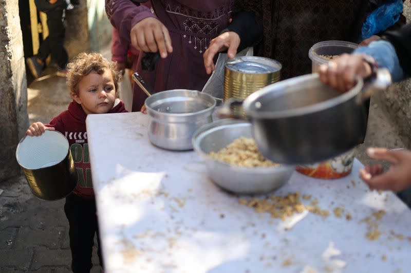 Palestinians wait to receive food cooked by a charity kitchen amid shortages, in Rafah