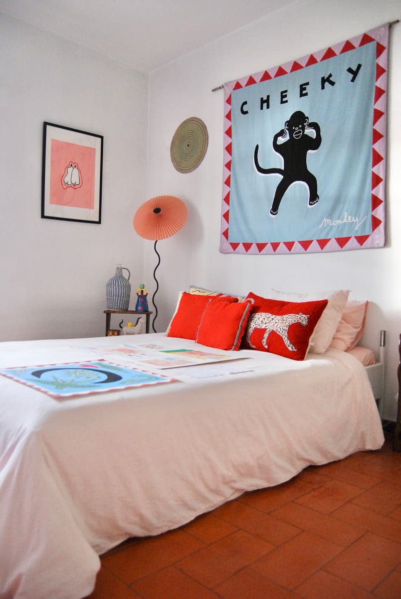 Cheeky monkey art tapestry hung above bed in white bedroom with rust flooring.