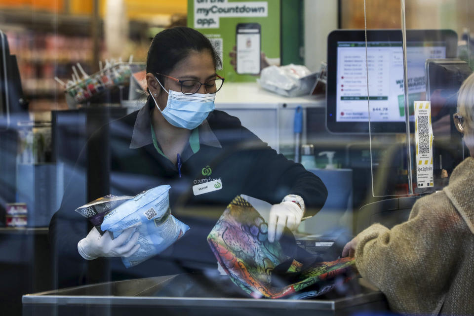 Supermarket staff help a customer with her shopping in Auckland, New Zealand, Tuesday, Aug. 17, 2021. New Zealand's government took drastic action Tuesday by putting the entire nation into a strict lockdown after detecting just a single community case of the coronavirus. (Hayden Woodward/New Zealand Herald via AP)