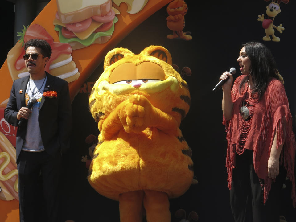 Un artista disfrazado como el personaje Garfield, centro, con los actores de doblaje Guillermo "Memo" Villegas, izquierda y Regina Orozco, derecha, en la alfombra naranja de la versión en español para Latinoamérica de "The Garfield Movie" en la Ciudad de México el domingo 28 de abril de 2024. (Foto AP/Berenice Bautista)