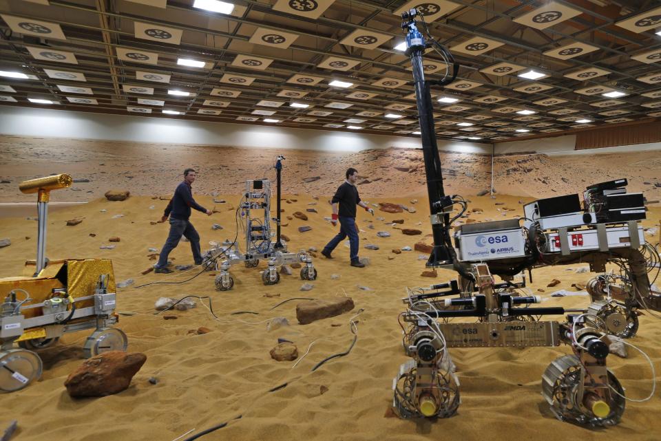 Personnel walk on the 'Mars Yard Test Area', a testing ground where robotic vehicles of the European Space Agency’s ExoMars program scheduled for 2018, are tested in Stevenage, England, Thursday, March 27, 2014. It looks like a giant sandbox - except the sand has a reddish tint and the “toys” on display are very expensive prototypes designed to withstand the rigors of landing on Mars. The scientists here work on the development of the autonomous navigation capabilities of the vehicle, so by being in communication with controllers on earth twice a day, will be able to use the transmitted information to navigate to new destinations on Mars. (AP Photo/Lefteris Pitarakis)