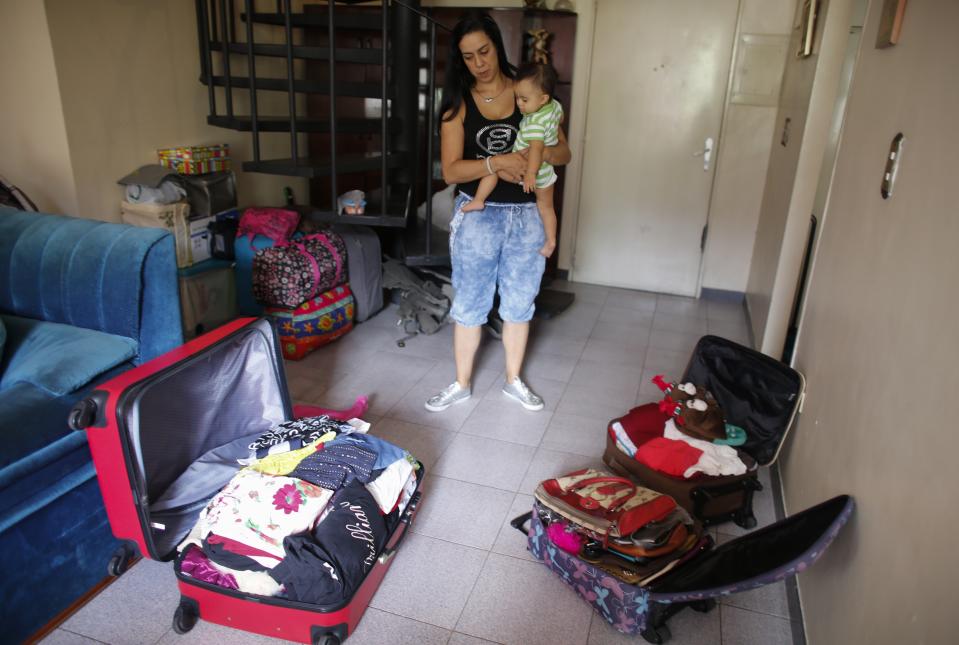 In this Oct. 31, 2019 photo, Yenika Calderon, 41, holds her 10-month-old baby Gael, while standing inside her apartment with suitcases packed with personal belongings to sell at a secondhand market, in Caracas, Venezuela. Deciding that it's time to abandon her crisis-torn homeland of Venezuela, Calderon hopes the money she makes will give her young family a fresh start far away in Spain. (AP Photo/Ariana Cubillos)