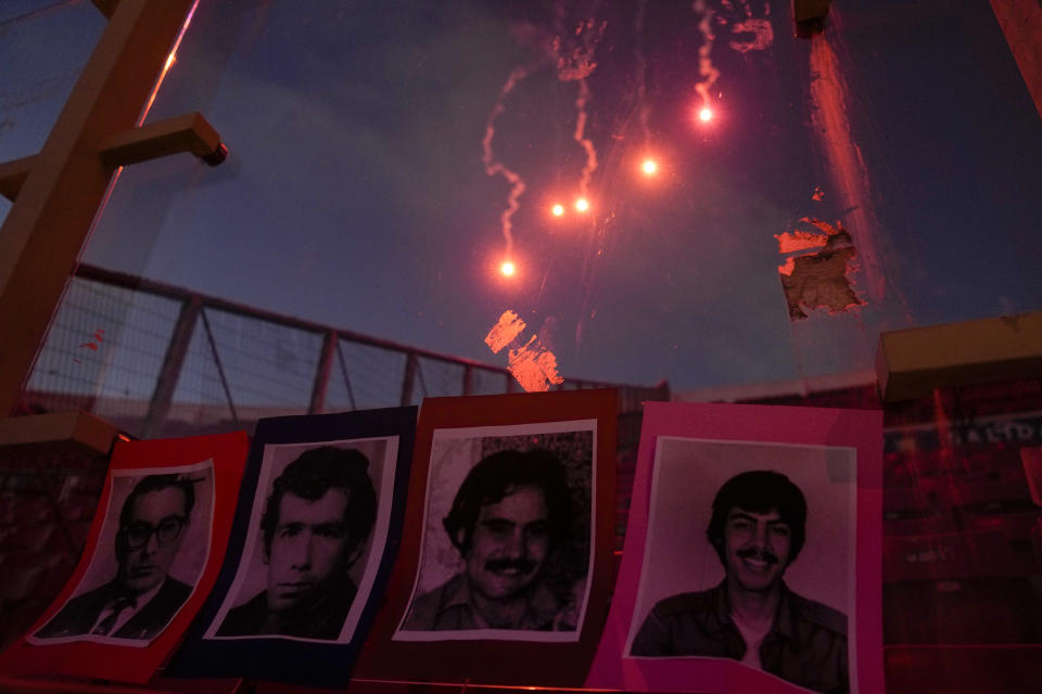 FILE - Fireworks light the sky while the portraits of persons who were disappeared and executed during the dictatorship led by Gen. Augusto Pinochet are displayed on the stands of the National Stadium, during a vigil marking the 50th anniversary of the 1973 military coup that toppled the government of late President Salvador Allende, in Santiago, Chile, Monday, Sept. 11, 2023. Despite the stadium’s dark past, many Chileans believe the Pan American Games offer a chance for redemption as the public learns more about what happened five decades ago. (AP Photo/Esteban Felix, File)