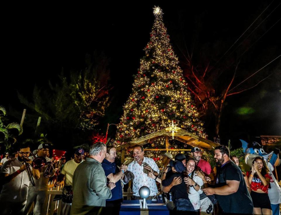 Nelson Albareda, presidente ejecutivo de Loud and Live; Javier Romero, y Tony Albelo, presidente ejecutivo de EngageLive (en el centro de la foto, de izquierda a derecha), se unen a otros mientras iluminan el árbol de Navidad en exhibición durante la noche de apertura de Christmas Wonderland en el Tropical Park, en Miami, el viernes 17 de noviembre de 2023.