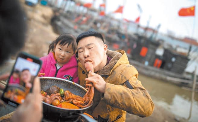 李加亮和他的女兒正在碼頭拍攝小視頻，他和女兒一起吃八爪魚。（宋嶠攝）