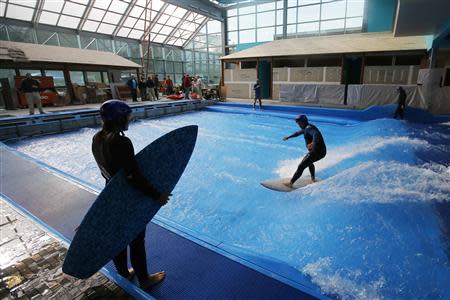 Todd Holland, former professional surfer on the world tour, tests the waves on a surfboard, as Lauren McLean (L) looks on, at the still under-construction Surf's Up indoor water and surf park in Nashua, New Hampshire November 15, 2013. REUTERS/Brian Snyder