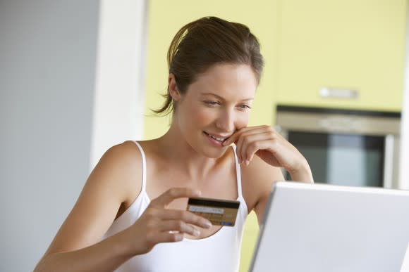 Woman holding a credit card in her right hand and smiling while looking at a laptop