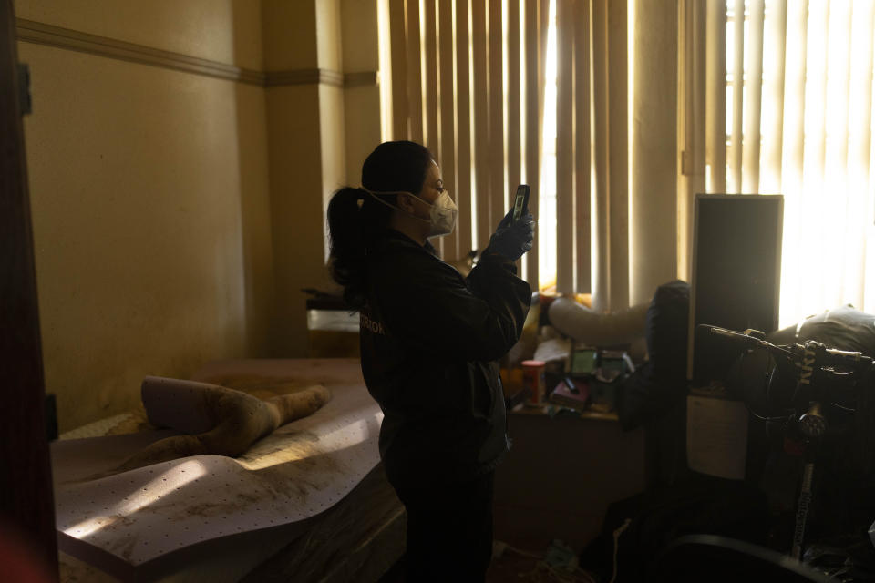 Standing next to a stained bed, Arusyak Martirosyan, an investigator with the Los Angeles County Public Administrator's office, records a scene with her smartphone while searching through a cluttered micro-apartment in Los Angeles, Wednesday, Dec. 13, 2023, where a tenant was found dead with no apparent next of kin. (AP Photo/Jae C. Hong)