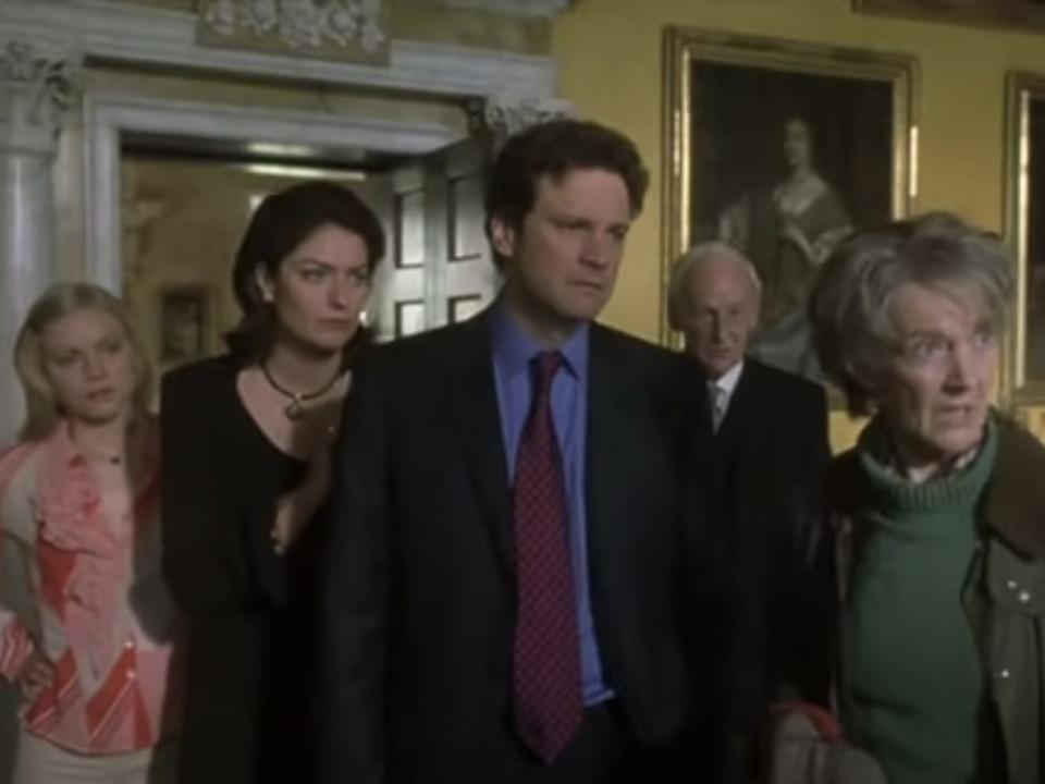 Colin Firth in a suit standing among other actors in "What a Girl Wants."