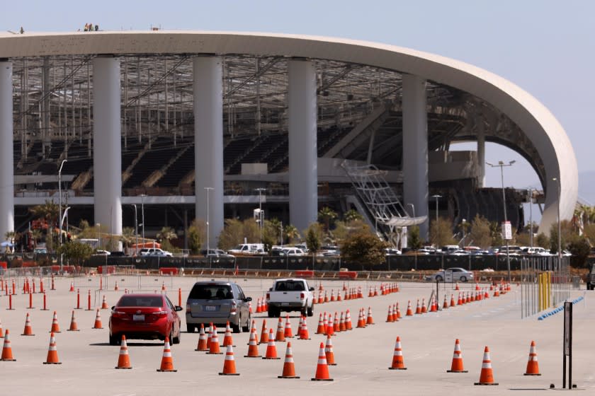 Cars exit the COVID-19 testing site at The Forum, with SoFi Stadium in the background.