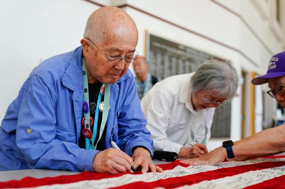 Minidoka survivor Paul Tomita, left, and wife Mabel Tomita, right, a survivor of Tule Lake and Gila River, sign a World War II-era 48-star flag as part of a project by Judge Johnny Gogo of Santa Clara County Superior Court at the College of Southern Idaho in Twin Falls. Gogo started the project to promote Fred Korematsu Day and has traveled around the country gathering signatures from survivors, filling several flags he has donated to Japanese American museums. Lindsey Wasson/AP