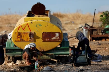 FILE PHOTO: Palestinians fill bottles with water from a tank outside their dwelling in Jordan Valley in the Israeli-occupied West Bank